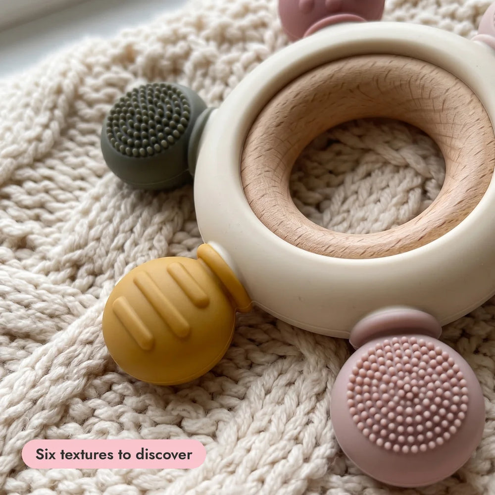 Close-up of the Sensory Teether's textured knobs and wooden ring on a knitted blanket